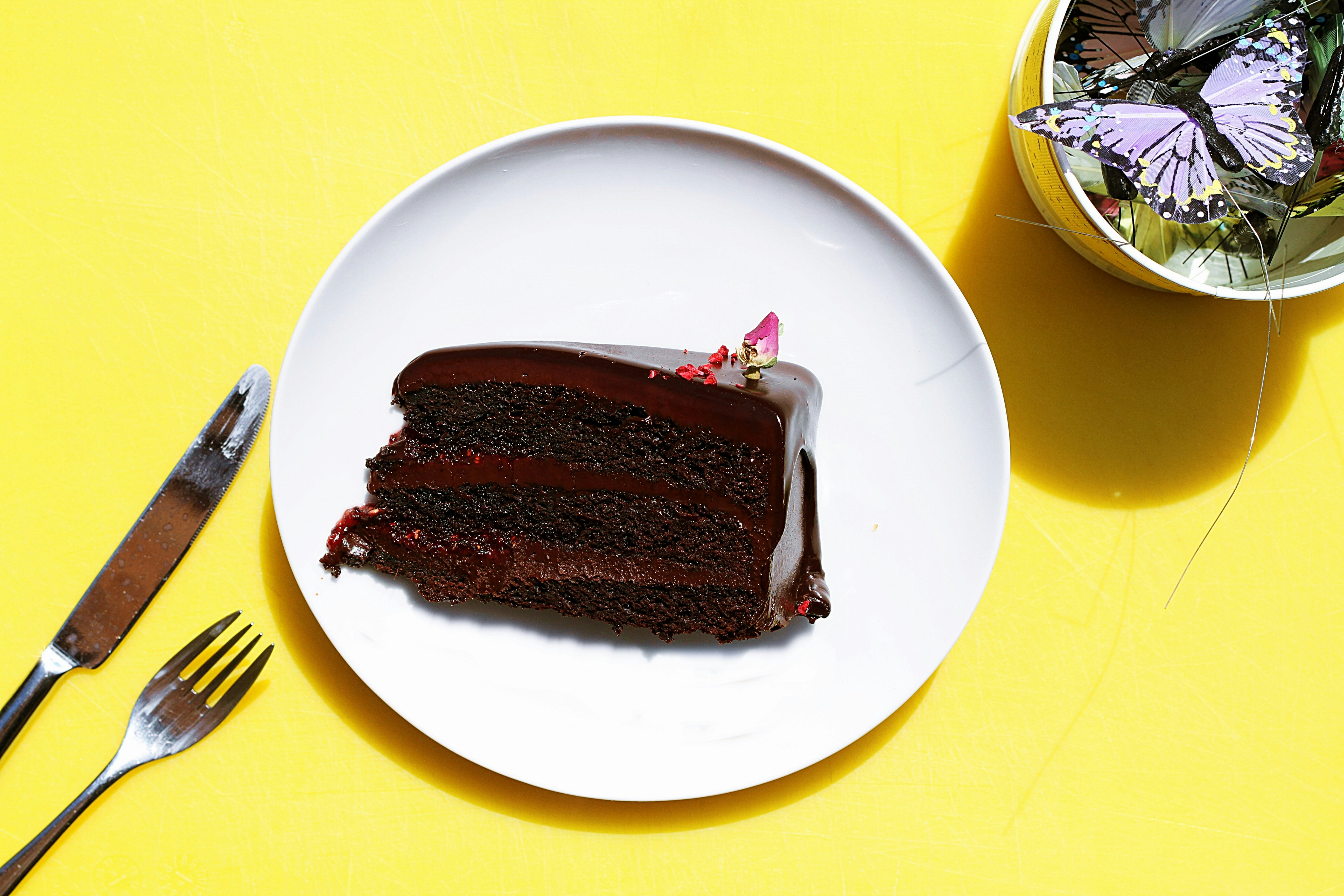 sliced chocolate moist cake in plate near gray stainless steel fork and knife